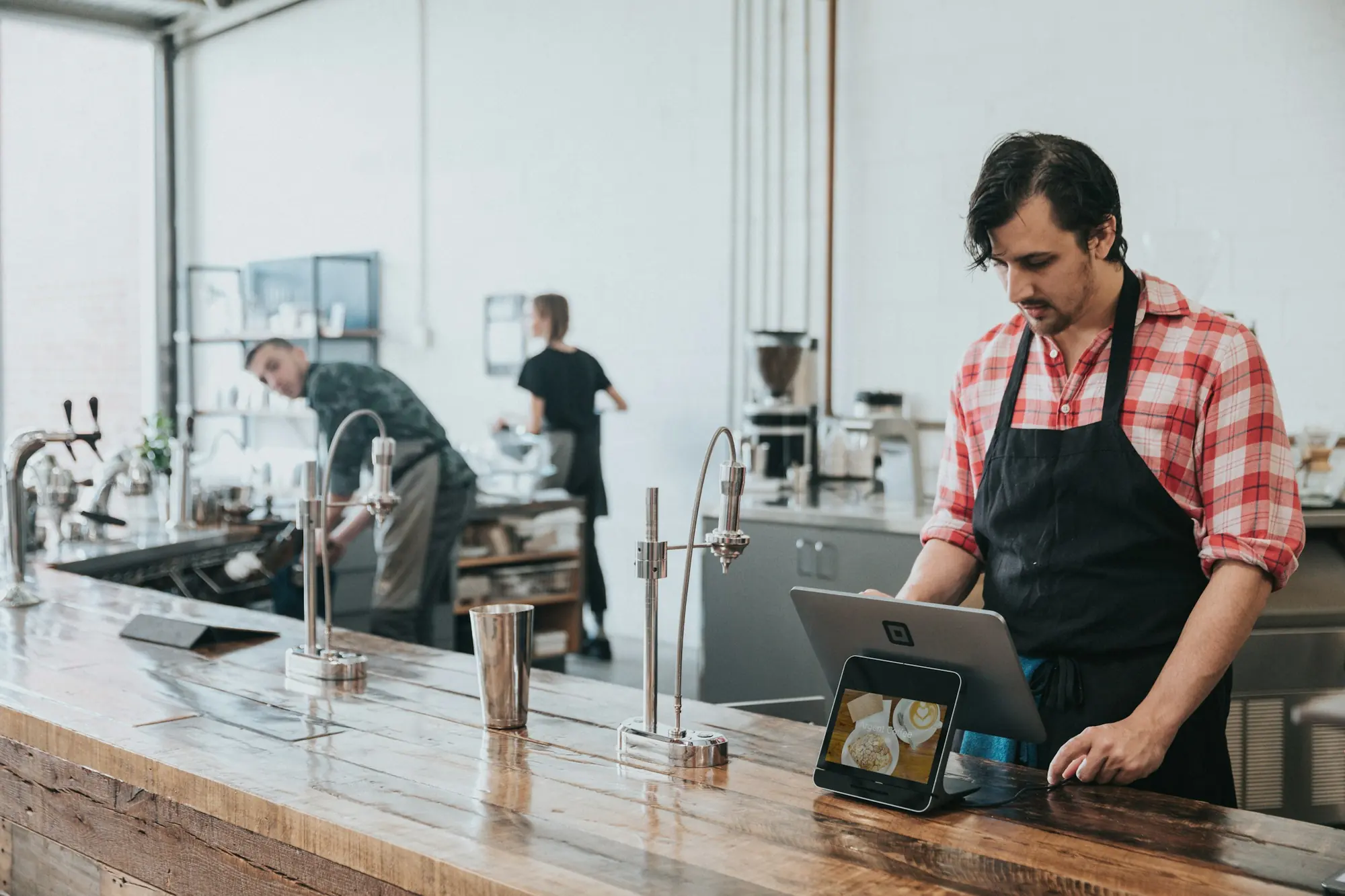 A barista checking orders on a tablet at a bright café counter